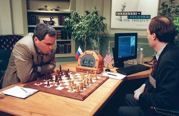 Gary Kasperov staring at a chessboard across the table from an operator playing for the Deep Blue AI.